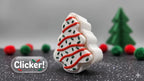 3D printed Christmas tree snack cake fidget clicker sitting on a dark surface with festive holiday decorations in the background
