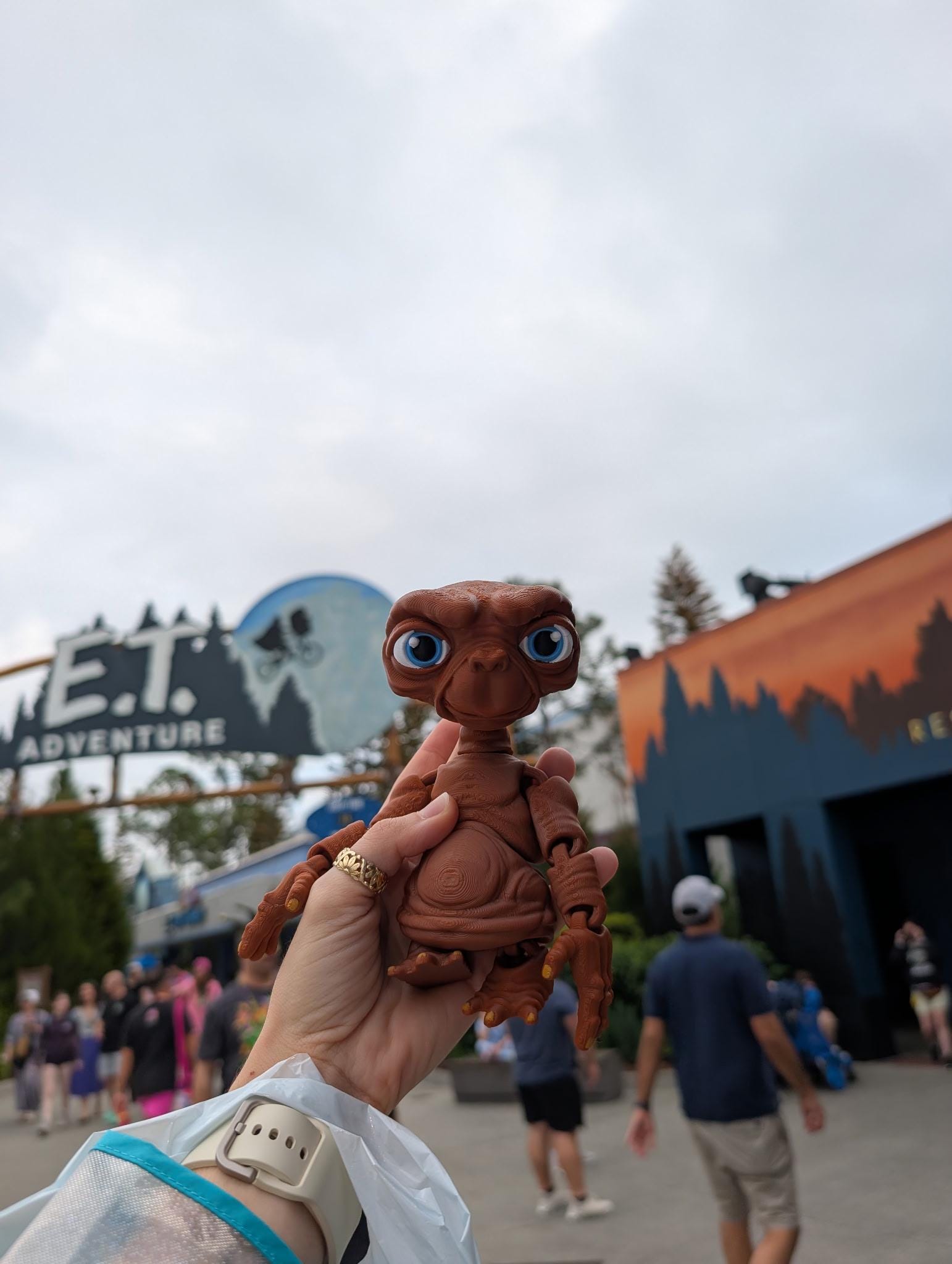 Person holding the 3D printed E.T. flexi figure in their hand with the E.T. Adventure theme park entrance in the background