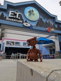 Full-color 3D printed E.T. flexi figure standing upright on a stone ledge in front of the E.T. Adventure theme park entrance