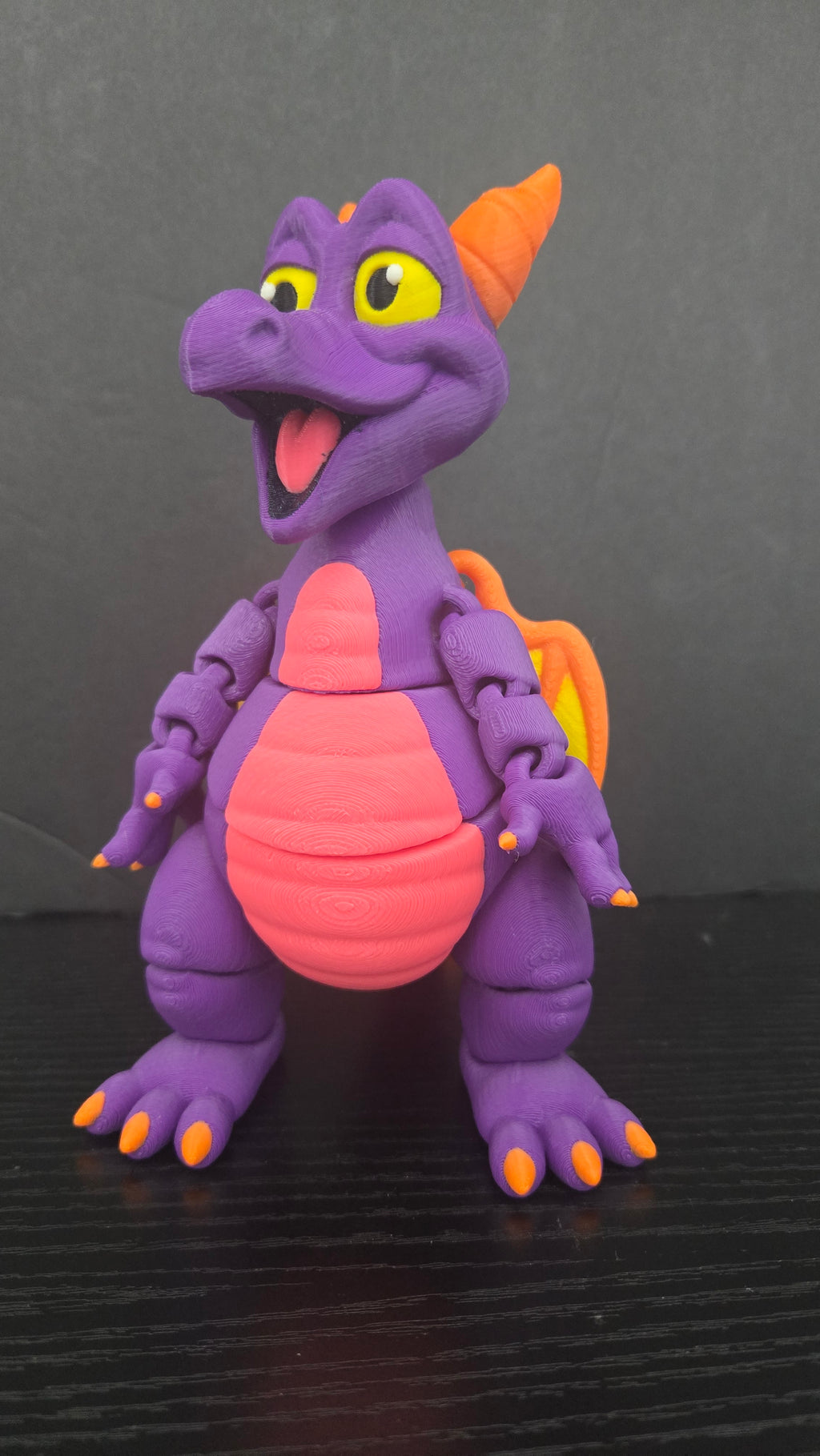 Front view of the Figment flexi figure on a dark studio surface showing its purple body and pink belly
