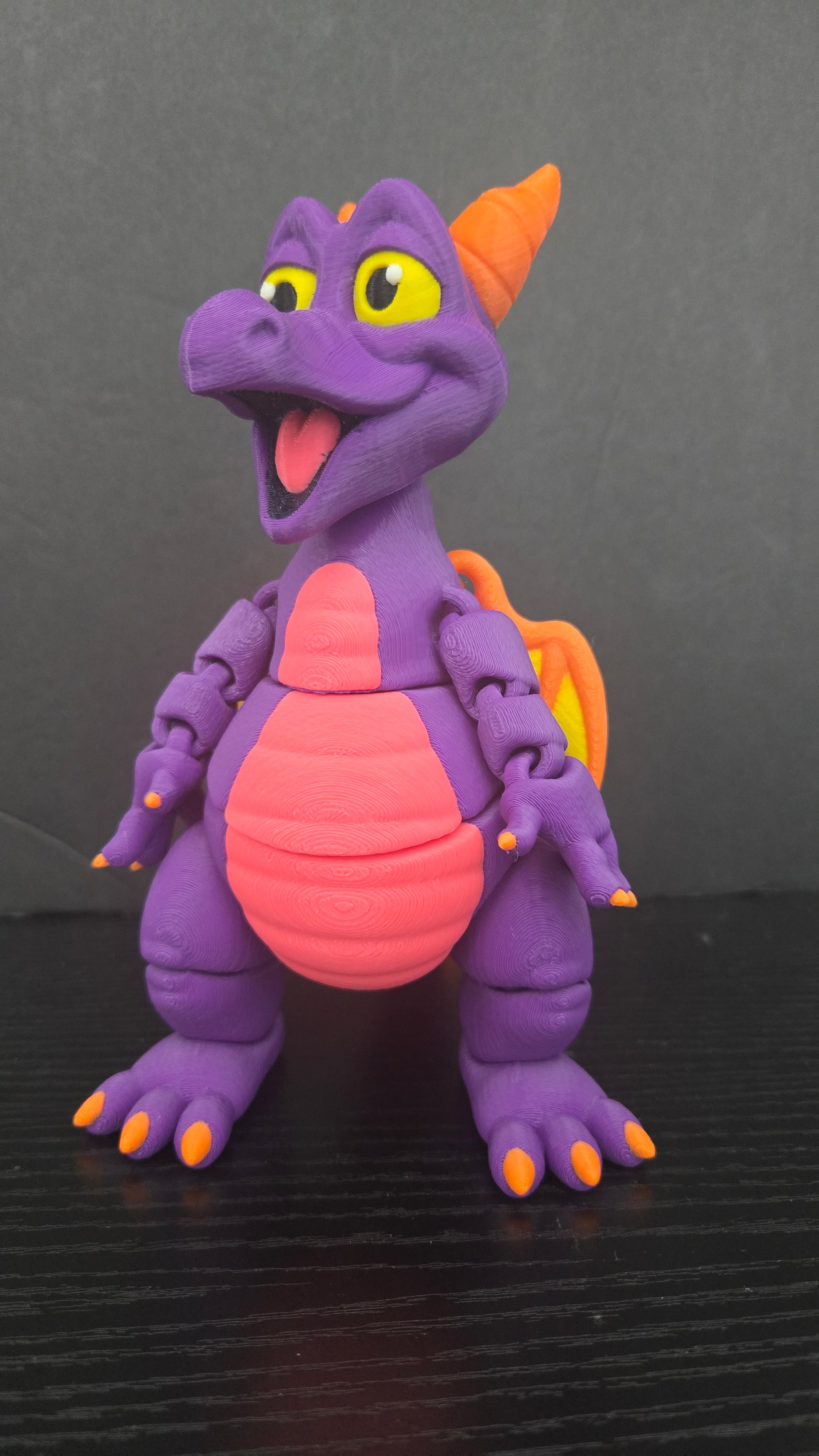 Front view of the Figment flexi figure on a dark studio surface showing its purple body and pink belly