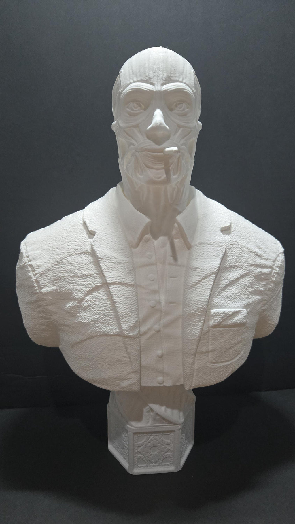 Straight front view of the unpainted white 3D printed Frank Cotton bust on a pedestal showing the raw face sinews and formal suit jacket