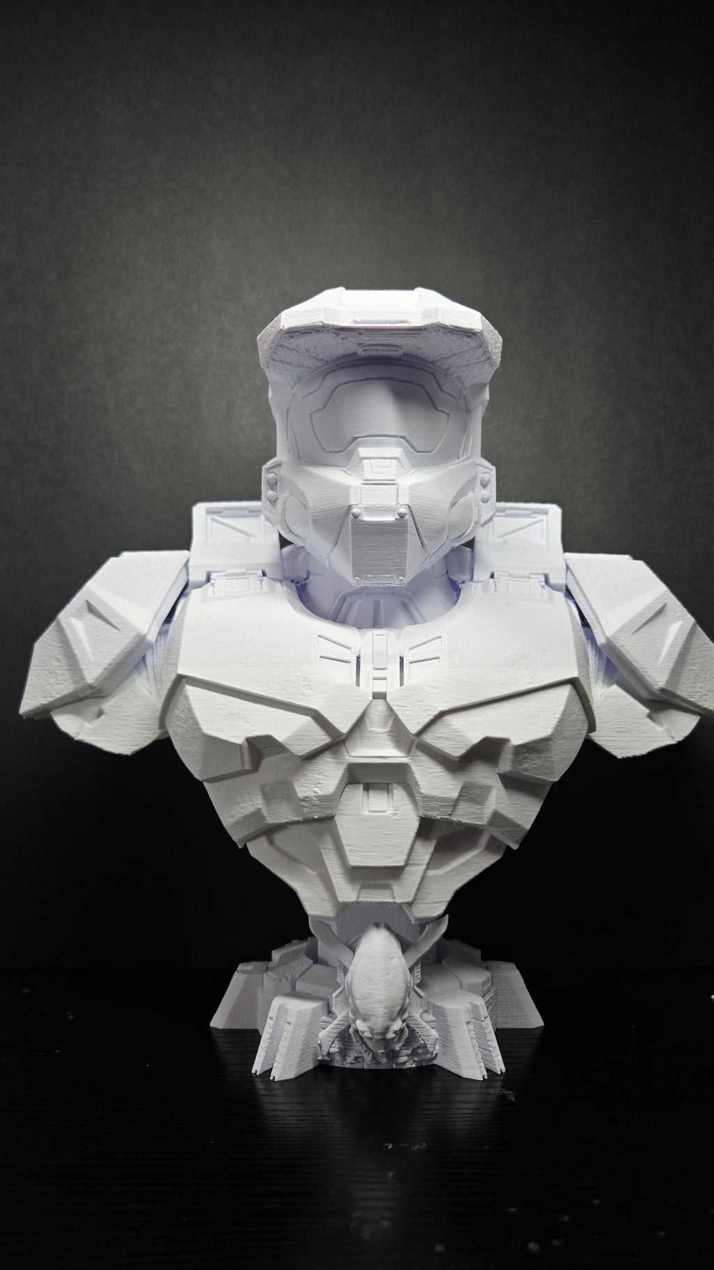 Unpainted white 3D printed Master Chief bust from Halo standing fully assembled on a black tabletop showing a complete front view