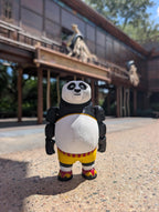 A hand holding up the 3D printed Kung Fu Panda Po flexi figure against a blurred background of Universal Studios theme park attractions