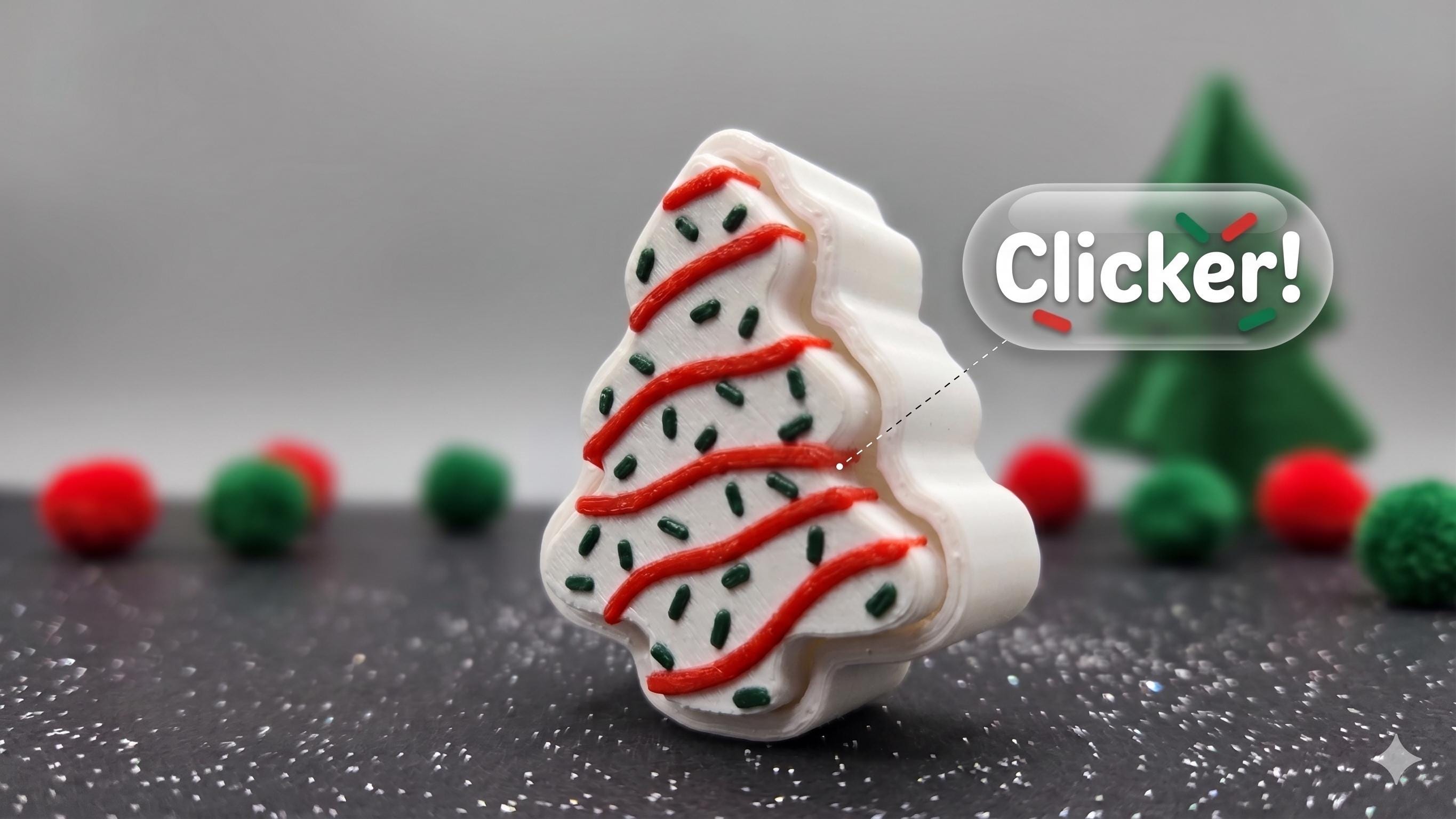 A Christmas tree-shaped white item with red and green decorative details, shown on a dark surface with blurred red and green pom-poms and a small green tree in the background. A 'Clicker!' badge appears on the right.