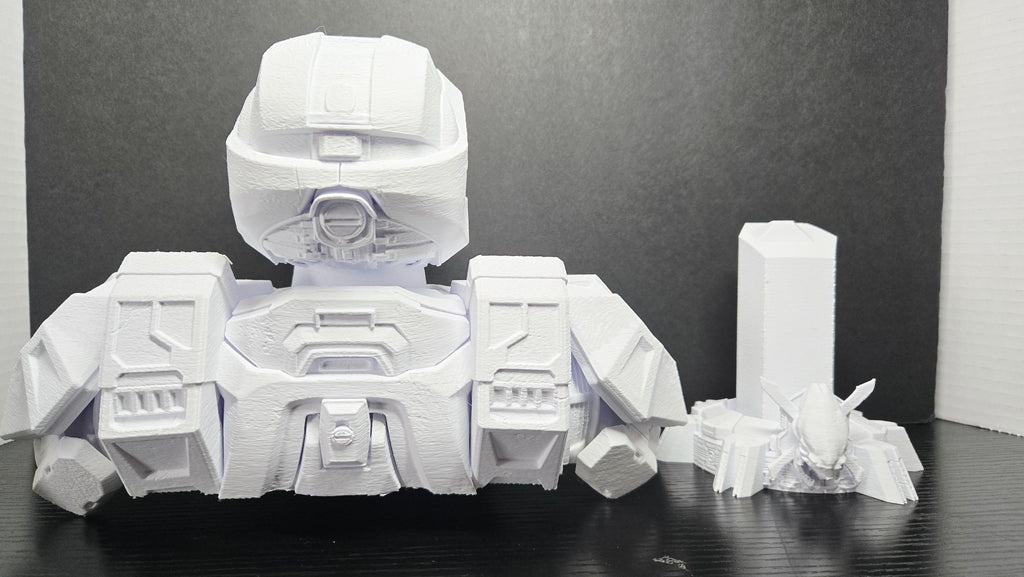 The 3D printed Master Chief bust disassembled into its three interlocking parts showing the armored torso, helmet, and detailed pedestal stand