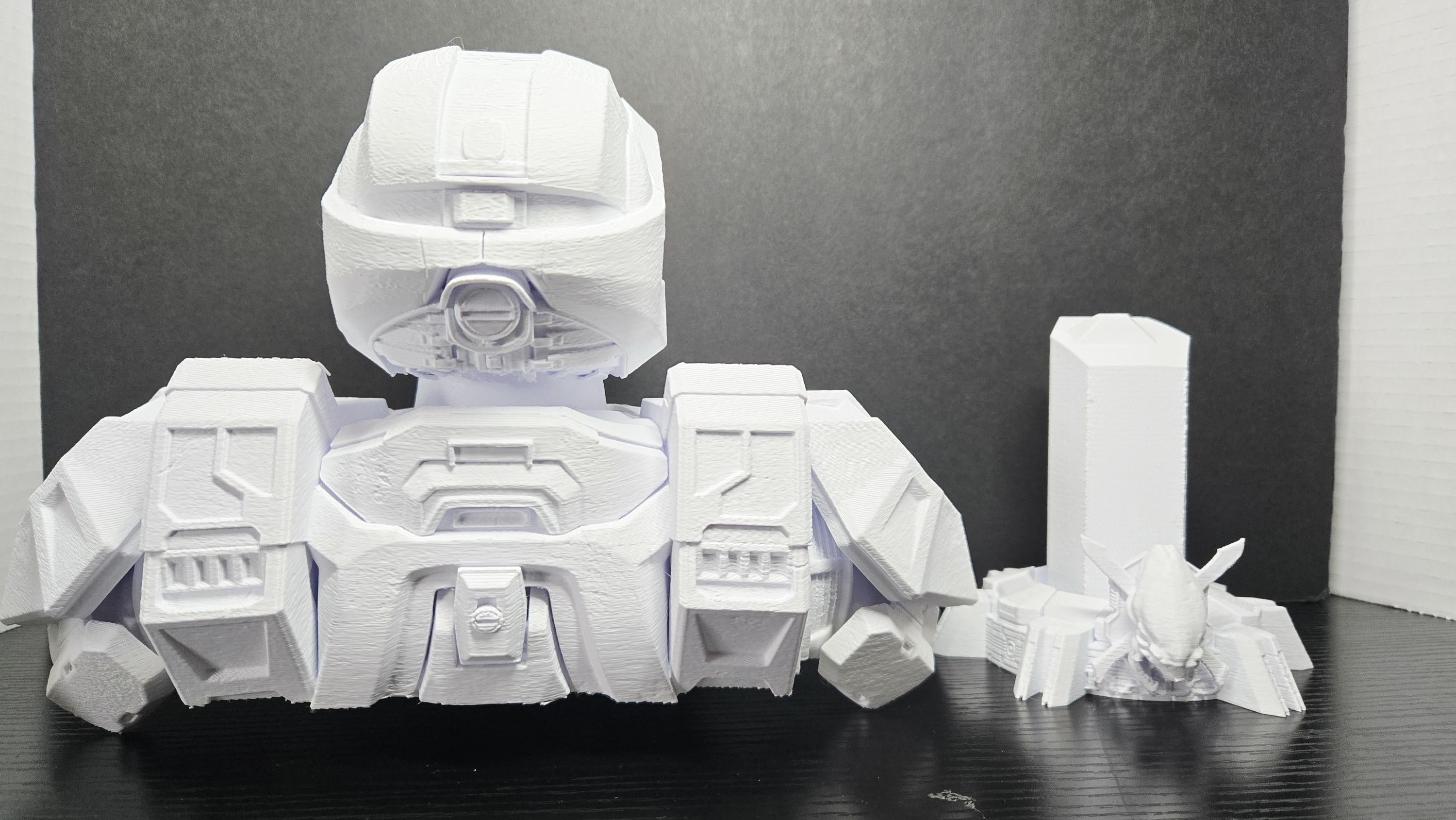 The 3D printed Master Chief bust disassembled into its three interlocking parts showing the armored torso, helmet, and detailed pedestal stand