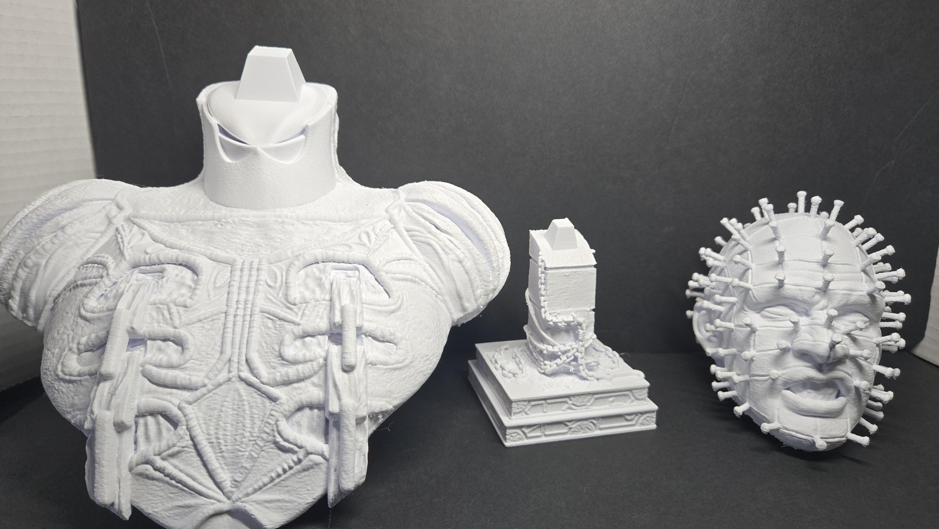 The 3D printed Pinhead bust disassembled into its three interlocking parts showing the torso, connector block, and head specimen