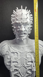 A vertical yellow measuring tape placed alongside the unpainted Pinhead bust to display the exact physical height of the model
