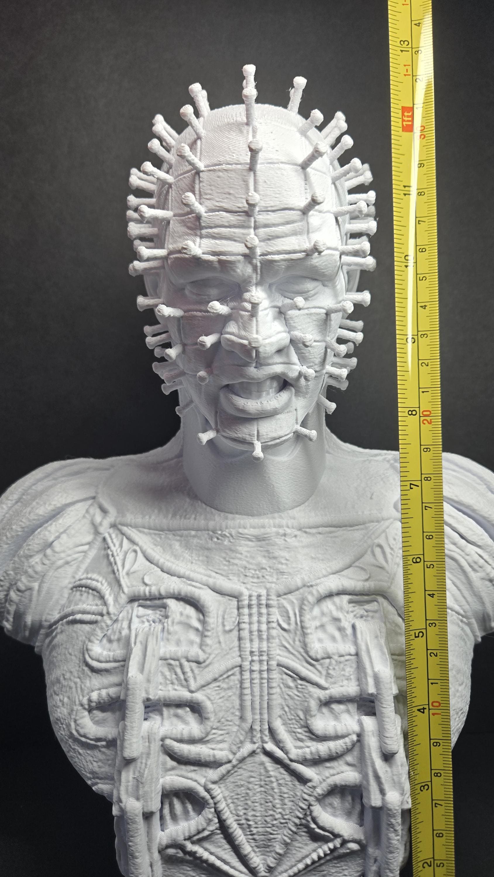 A vertical yellow measuring tape placed alongside the unpainted Pinhead bust to display the exact physical height of the model