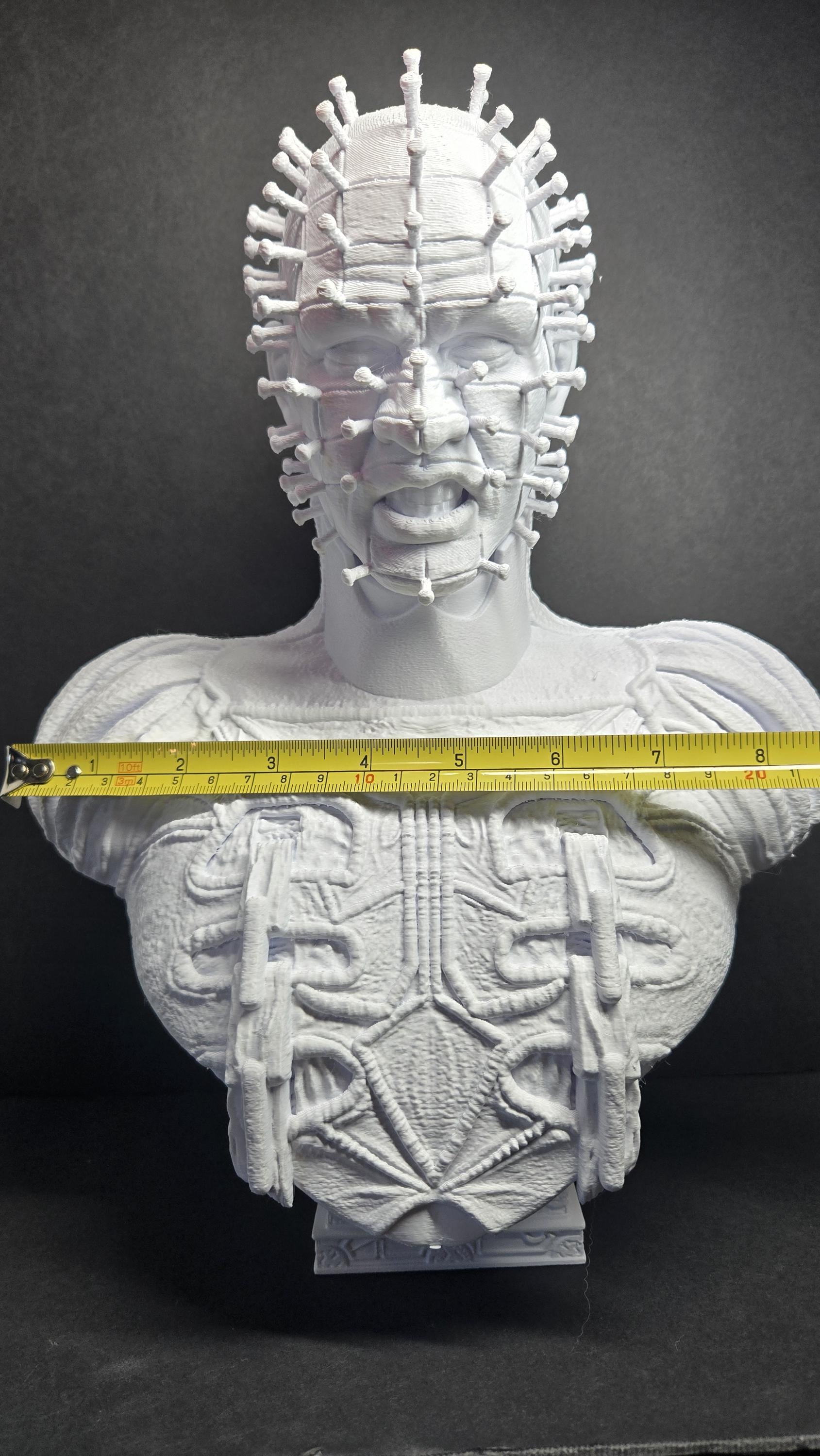 A horizontal yellow measuring tape placed across the shoulders of the unpainted Cenobite bust to show the exact physical width