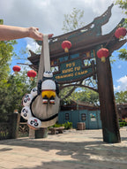 The articulated Kung Fu Panda Po figure being flexed and held up high with a scenic Universal Studios theme park walkway in the background