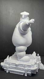 Side profile view of the unpainted Stay Puft Marshmallow Man statue highlighting the round body shape and street-level diorama base