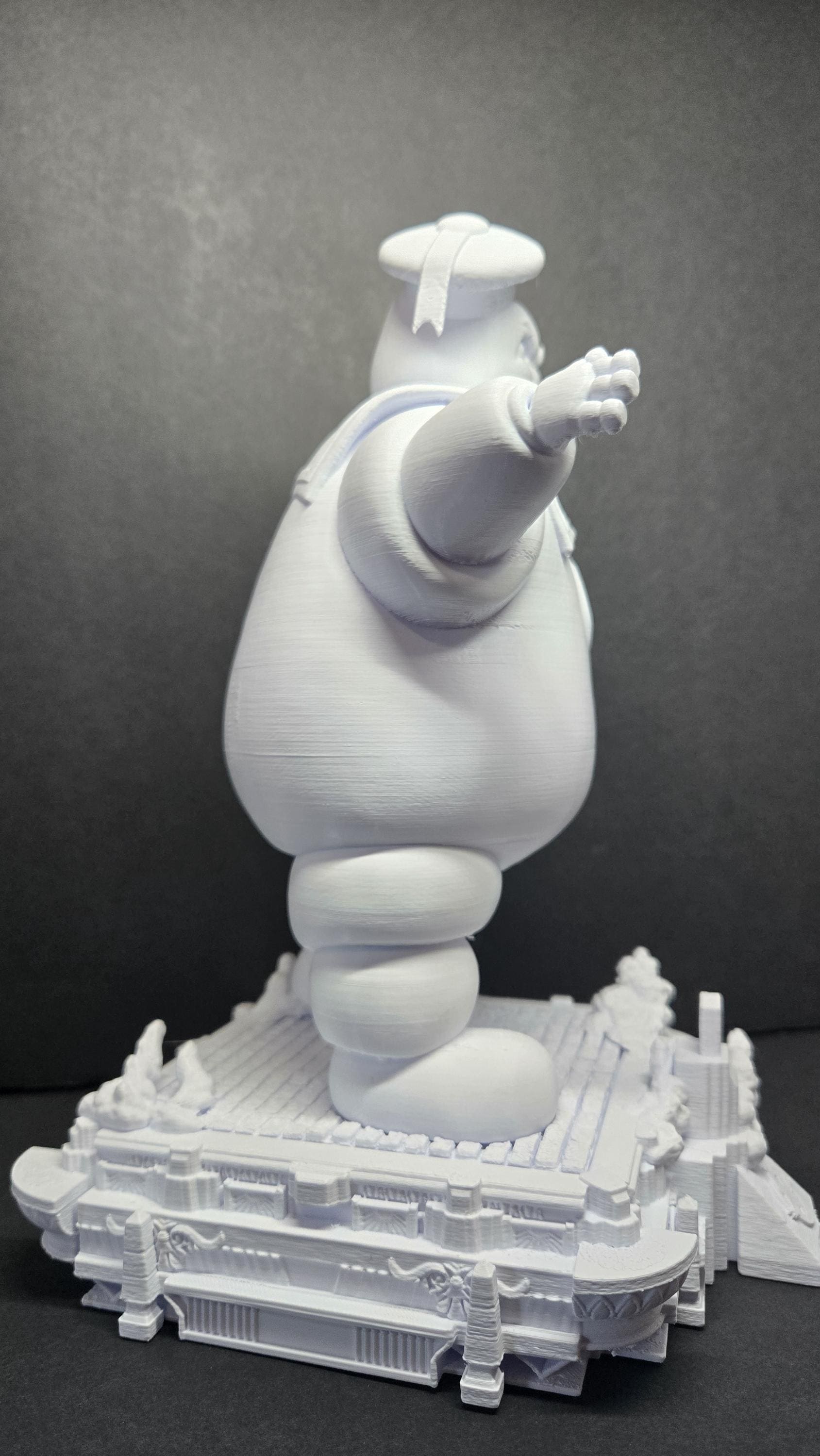 Side profile view of the unpainted Stay Puft Marshmallow Man statue highlighting the round body shape and street-level diorama base