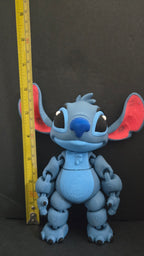 3D printed Stitch flexi figure standing next to a yellow measuring tape to demonstrate its display scale