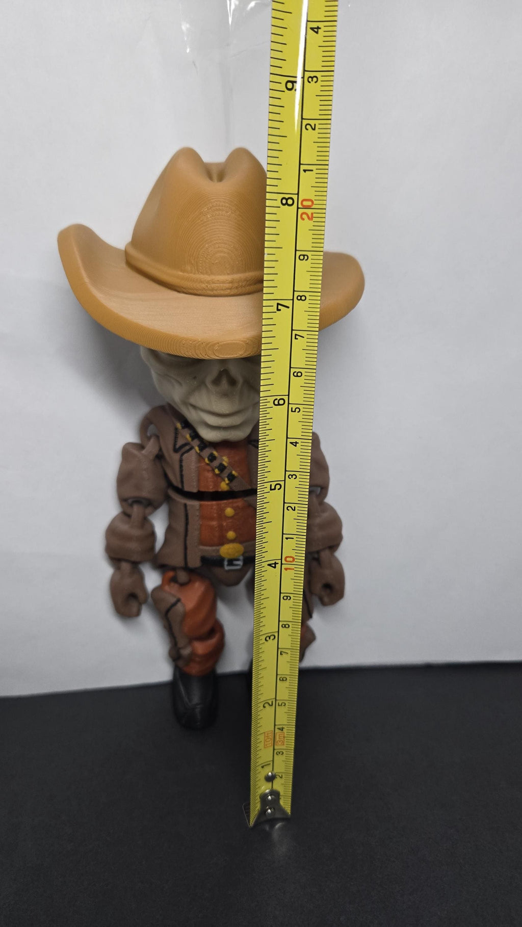 A vertical yellow measuring tape placed alongside the standing multi-color The Ghoul flexi figure to display its exact physical height