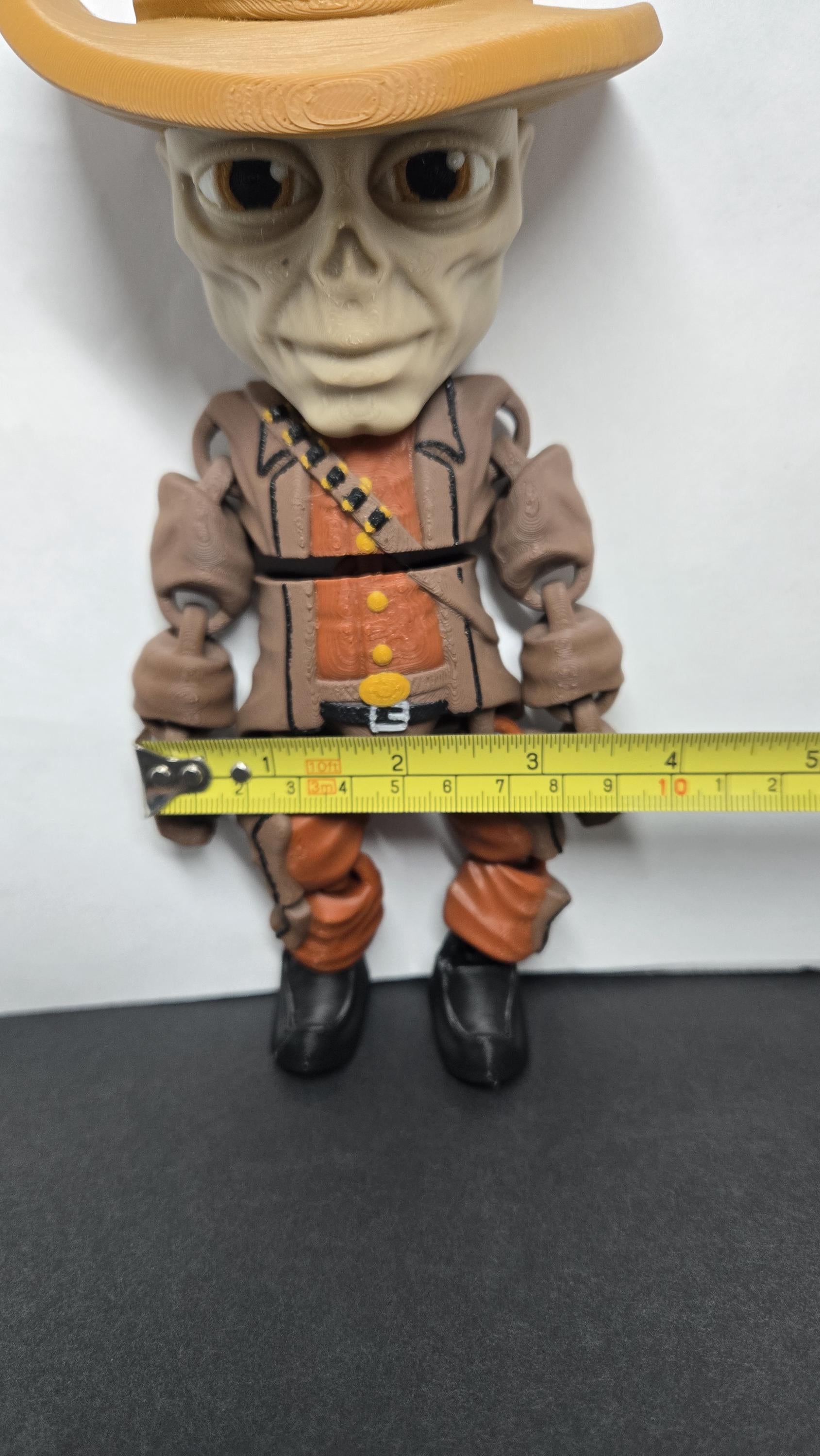 A horizontal yellow measuring tape placed across the arms of The Ghoul flexi figure to display its exact physical width