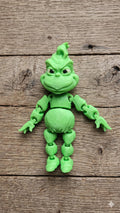 Full-color 3D printed grumpy holiday star flexi figure standing on a rustic wooden desk surface
