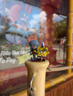 The 3D printed cartoon mini-figure set displayed on a wooden surface with a cartoon-themed store window in the background